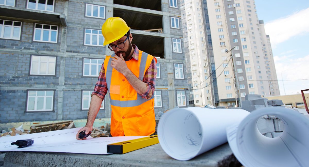 Pensive worker in hardhat and uniform looking at sketch of new building